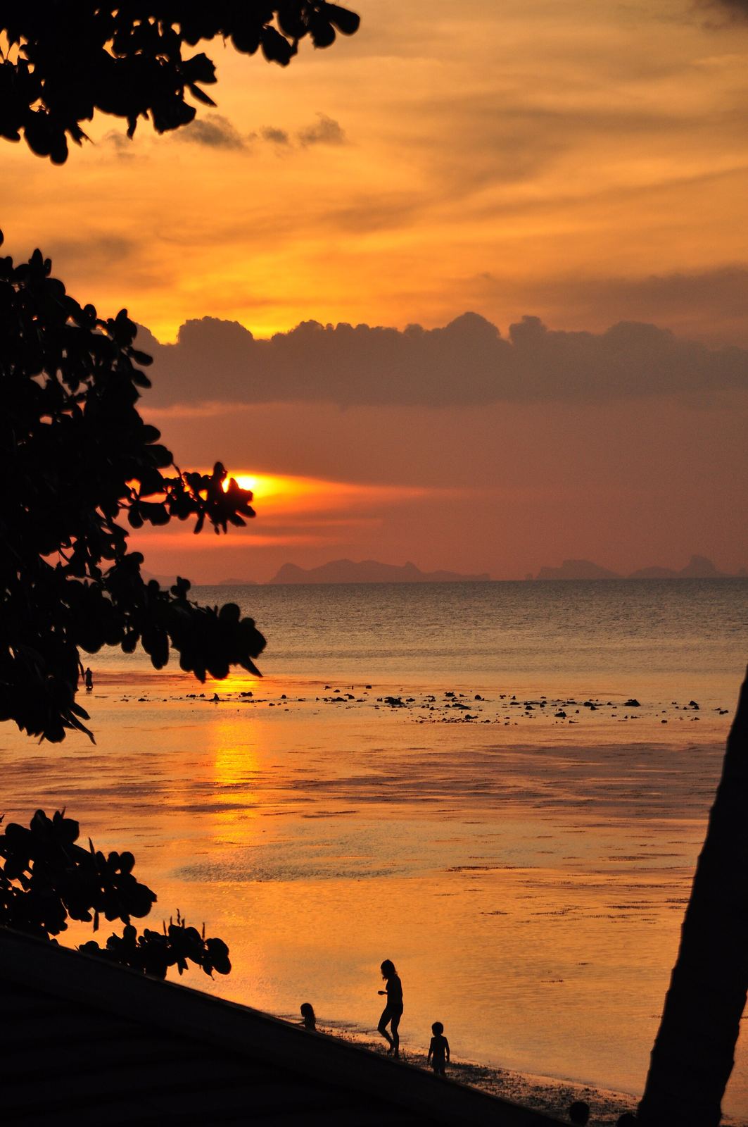 The sun setting into the Gulf of Thailand at Haad Yao beach, Koh Phangan, with people silhouetted on the sand