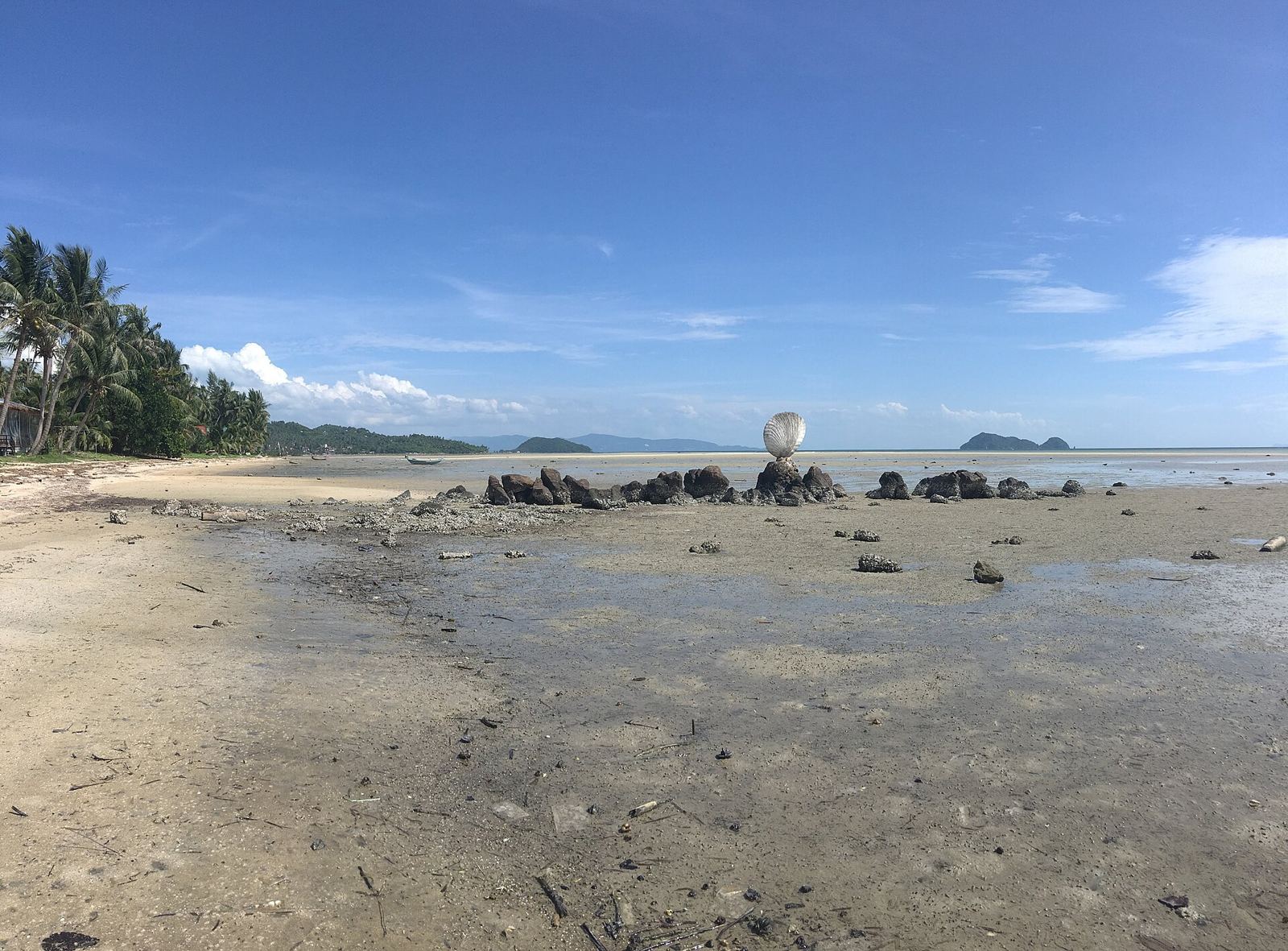 Hin Kong beach on Koh Phangan at low tide, with wet sand and rocks stretching out towards the sea
